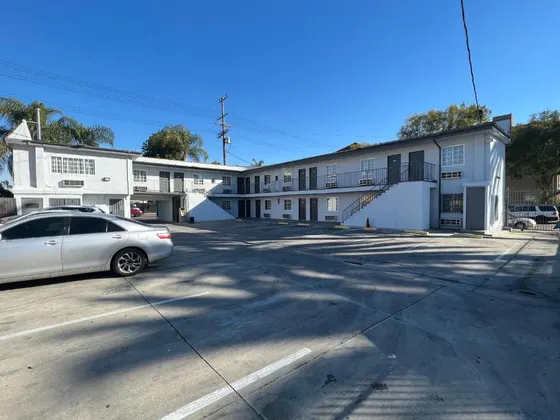 Two-story white motel surrounding a sunny parking courtyard