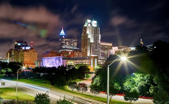 Raleigh skyline lit at night above highway light trails