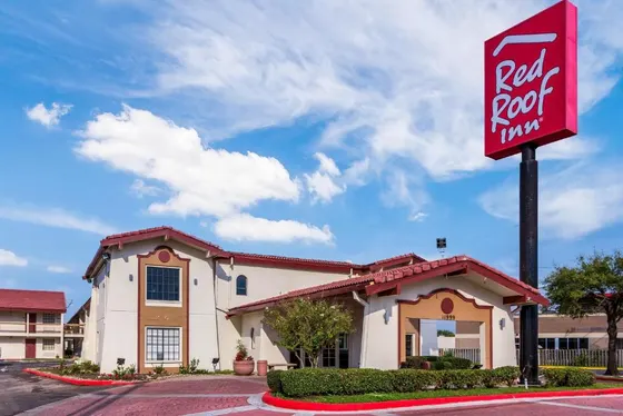 White motel with a red tile roof and tall red sign