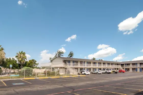 White two-story motel with blue doors, a fenced pool, and parking