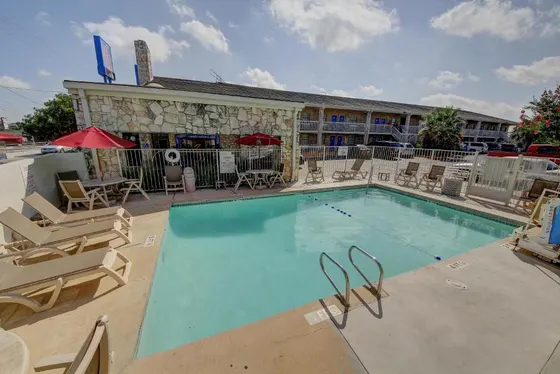 Outdoor pool with tan lounge chairs and a white fence