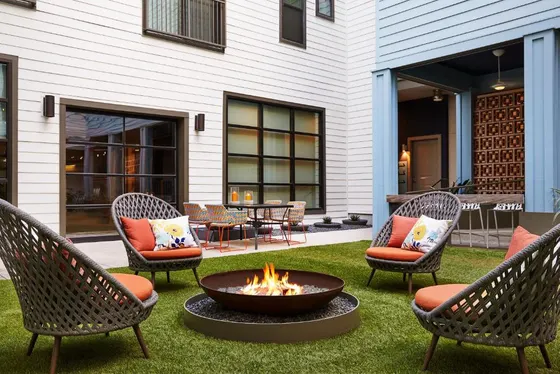 Woven chairs with orange cushions around a courtyard fire pit