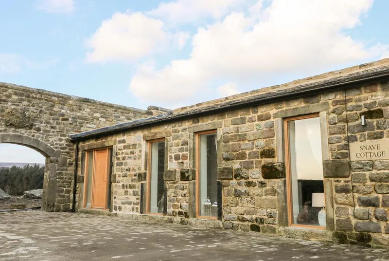 Snave Cottage stone frontage with arch and name sign under blue sky