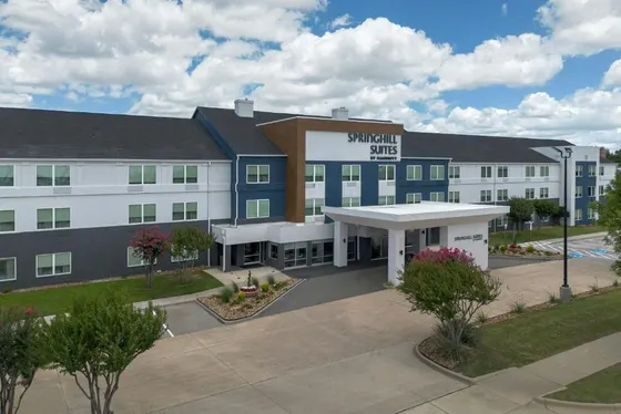 White and gray hotel with a white canopy and pink flowering trees