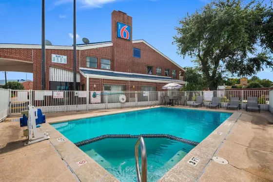 Pool with lounge chairs in front of a brick Motel 6