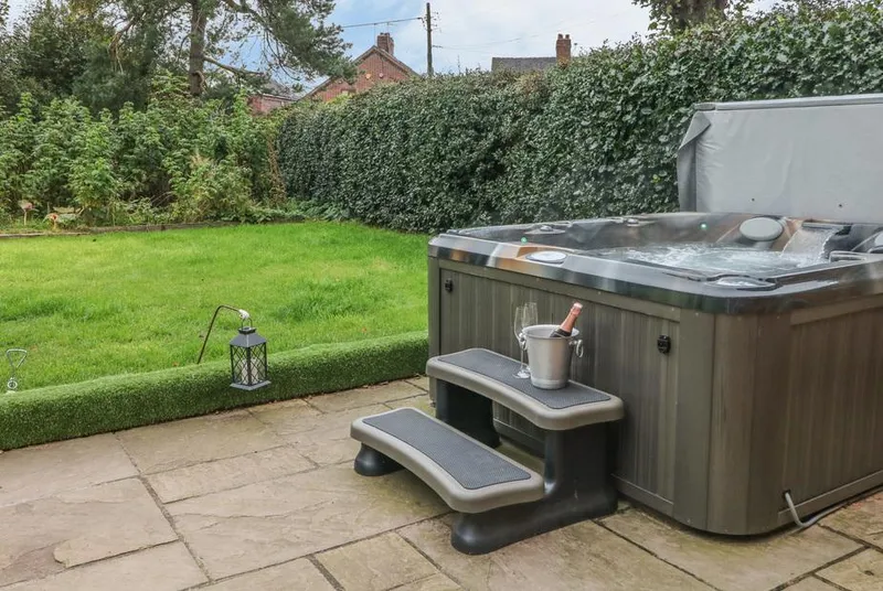 Orchard Barn hot tub on patio with champagne styling and green garden