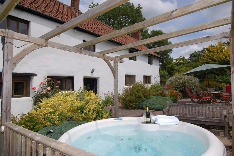 Surridge Farmhouse hot tub with champagne under pergola and farmhouse backdrop