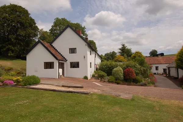 Surridge Farmhouse white-rendered exterior with lawn and green hills behind