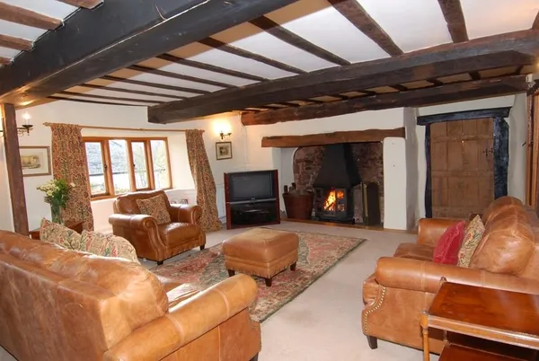 Surridge Farmhouse beamed living room with lit wood-burning stove in stone inglenook