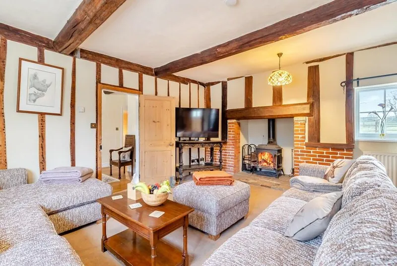 Sycamore Farmhouse living room with lit wood burner and exposed timber framing