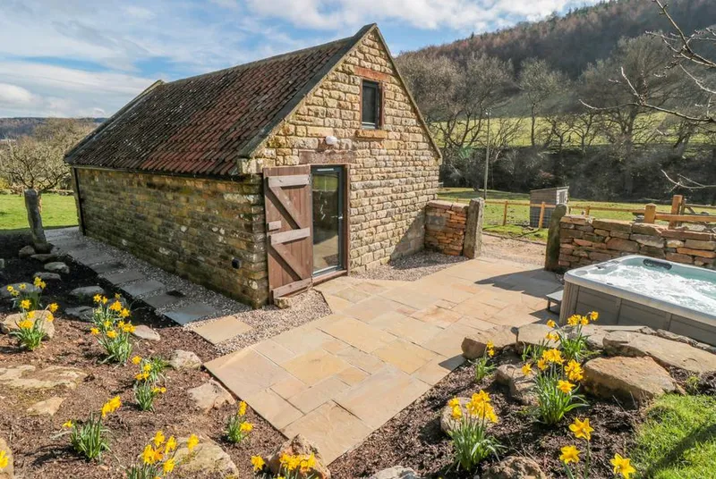 Thompson Rigg Barn honey stone barn with patio and daffodils