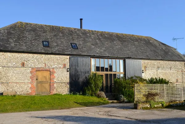 The Barn front facade with flint walls and glazed entrance under blue sky