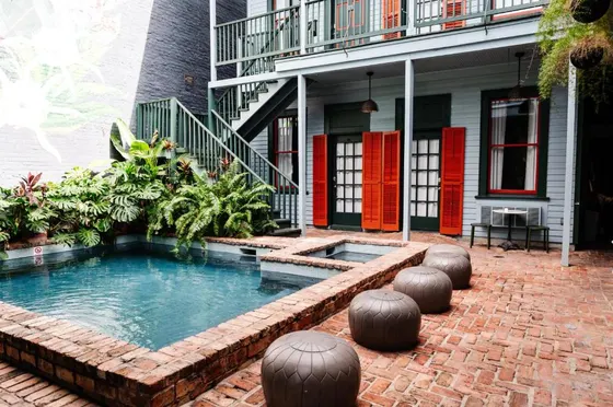 Brick courtyard pool with grey poufs and red shutters
