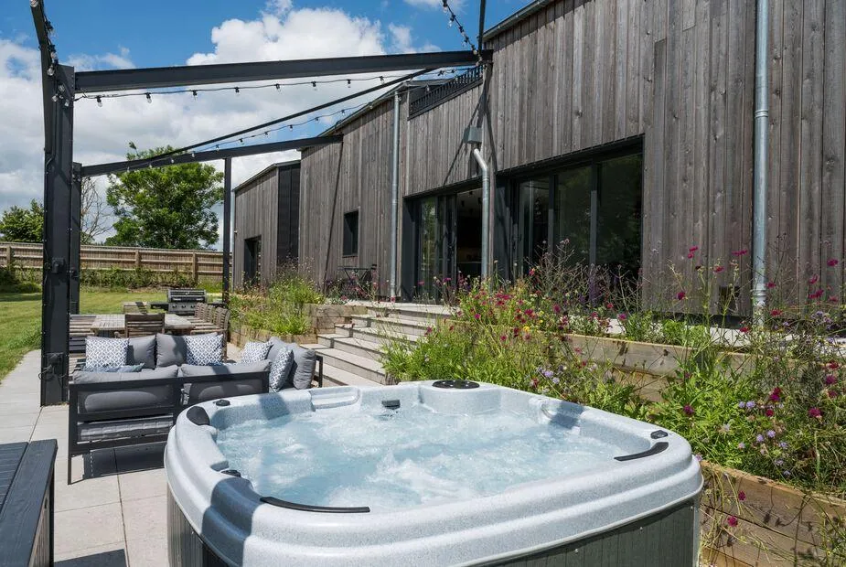 The Grain Store hot tub with wildflowers and timber-clad property behind