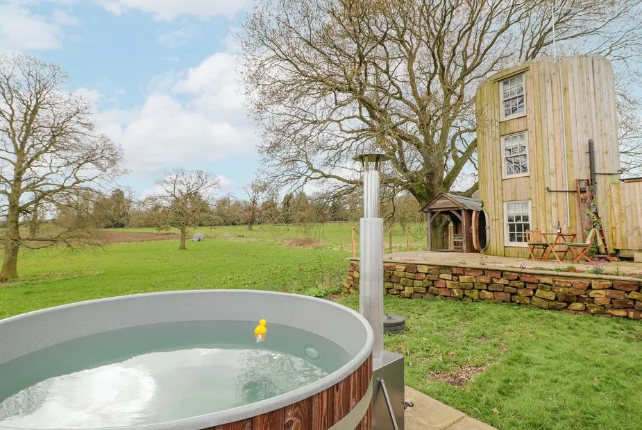 The Lazy Squire wood-fired hot tub with property tower and countryside behind