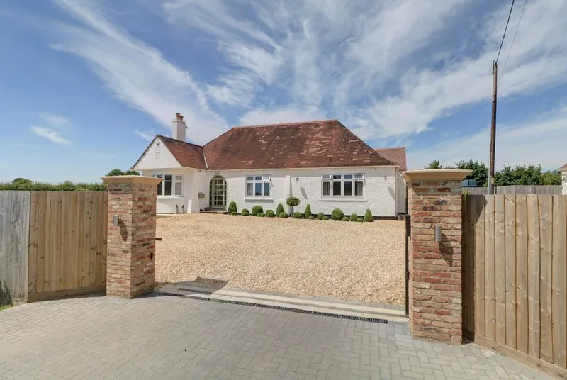 The Little Paddock white bungalow through gated entrance with blue sky