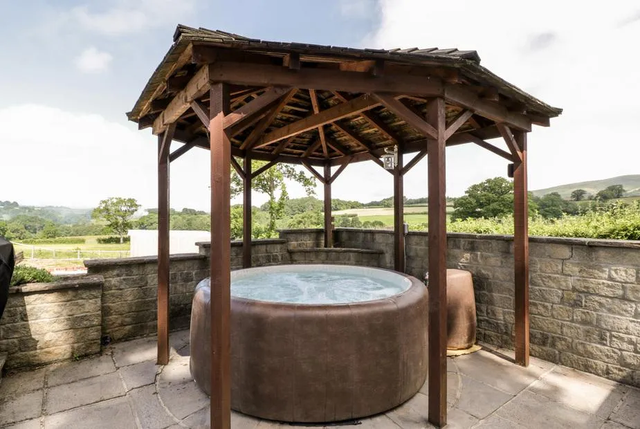 The Stables hot tub under wooden gazebo with rolling countryside hills