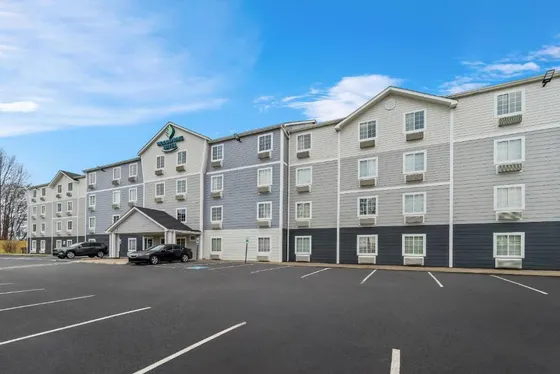 Four-story gray hotel exterior and parking lot beneath a blue sky