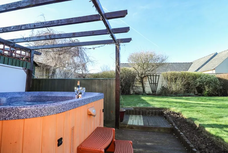 Y Stabl hot tub under the pergola beside the sunny lawn