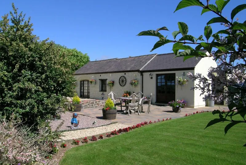 Y Stabl cottage exterior with manicured lawn and flower-filled patio